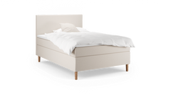 Beige stoppad enkelsäng med vit täcke och kudde, träben, frilagd mot svart bakgrund.