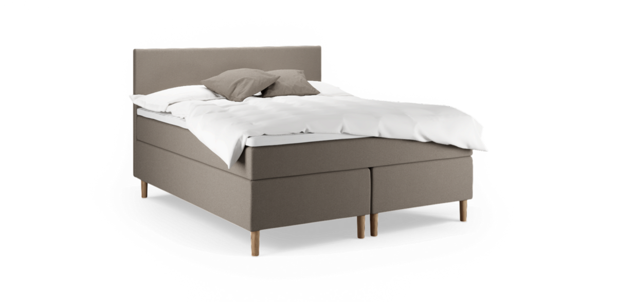 Beige stoppad kontinentalsäng med träben, vit bäddning och två grå kuddar, fotad snett framifrån på neutral bakgrund.