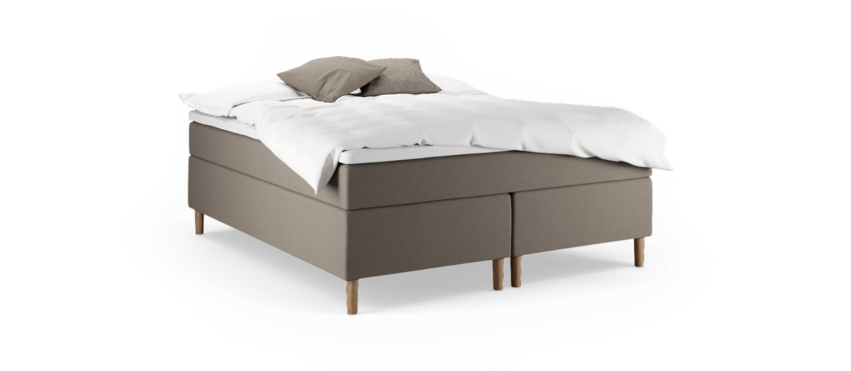 Beige kontinentalsäng med vit bäddning och två kuddar på träben, fotograferad i studio mot svart bakgrund.