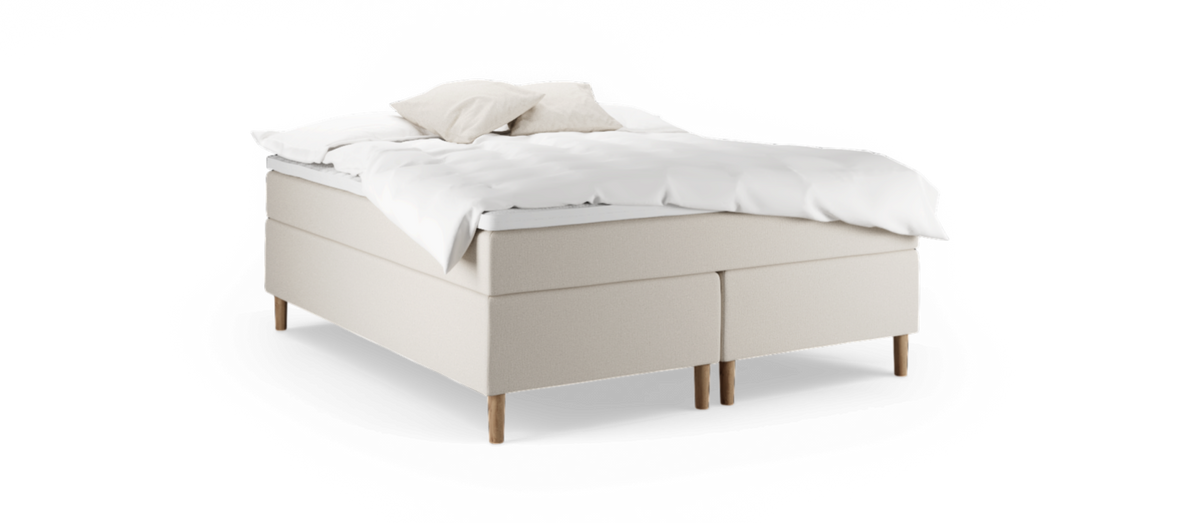 Beige kontinentalsäng med träben och vita sängkläder, två kuddar ovanpå.