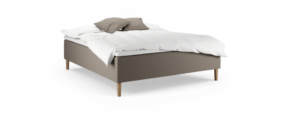 Klädd säng med träben, vit bäddning och två beige kuddar mot svart bakgrund.