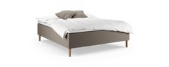 Klädd säng med träben, vit bäddning och två beige kuddar mot svart bakgrund.