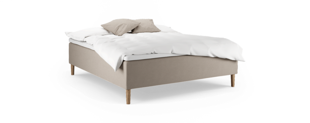 Beige stoppad säng med träben, vitt täcke och två beiga kuddar, frilagd mot svart bakgrund.