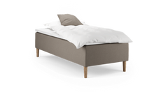 Enkel enkeltsäng med beige klädd sängbas, vit kudde och täcke samt träben, frilagd på vit bakgrund.