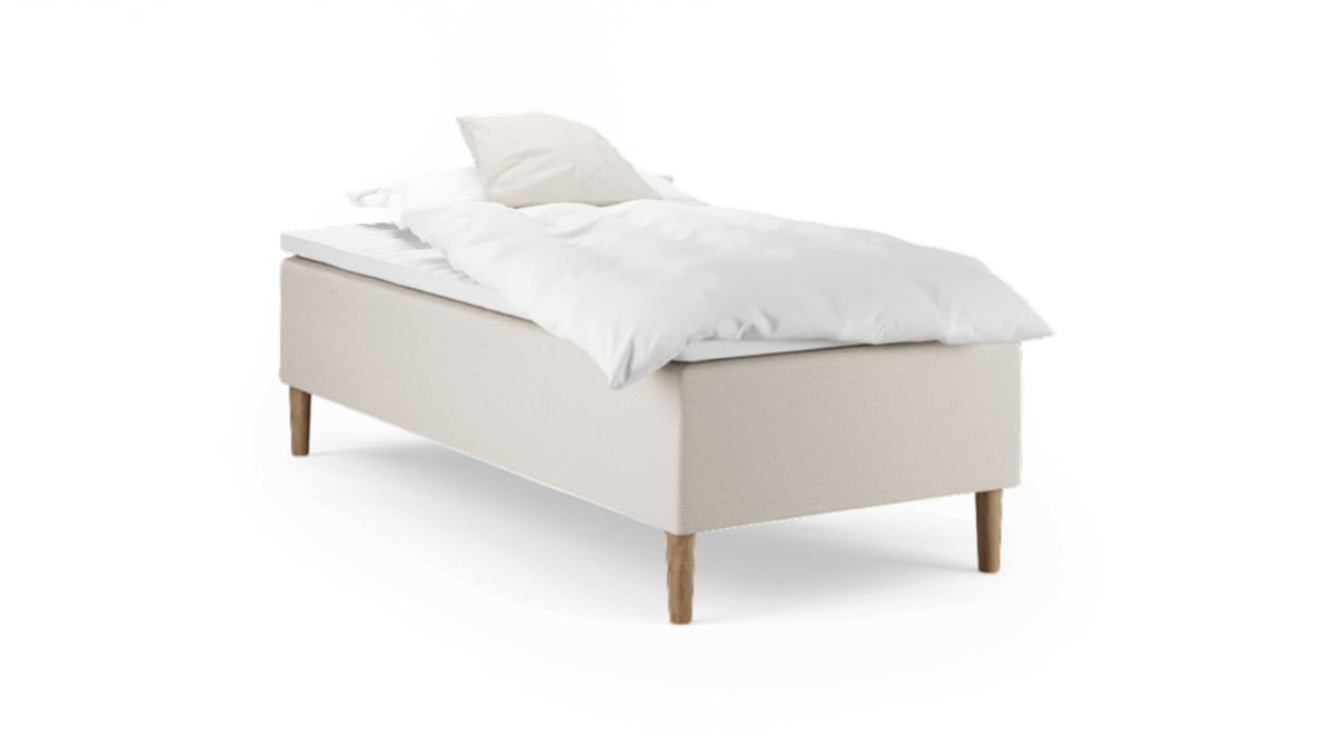 Enkelbädd med beige klädd sängbas, träben och vit bäddning med kudde.