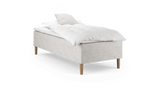 Enkelbädd med ljusbeige tygklädd bas, träben samt vit kudde och täcke, frilagd mot svart bakgrund._ps