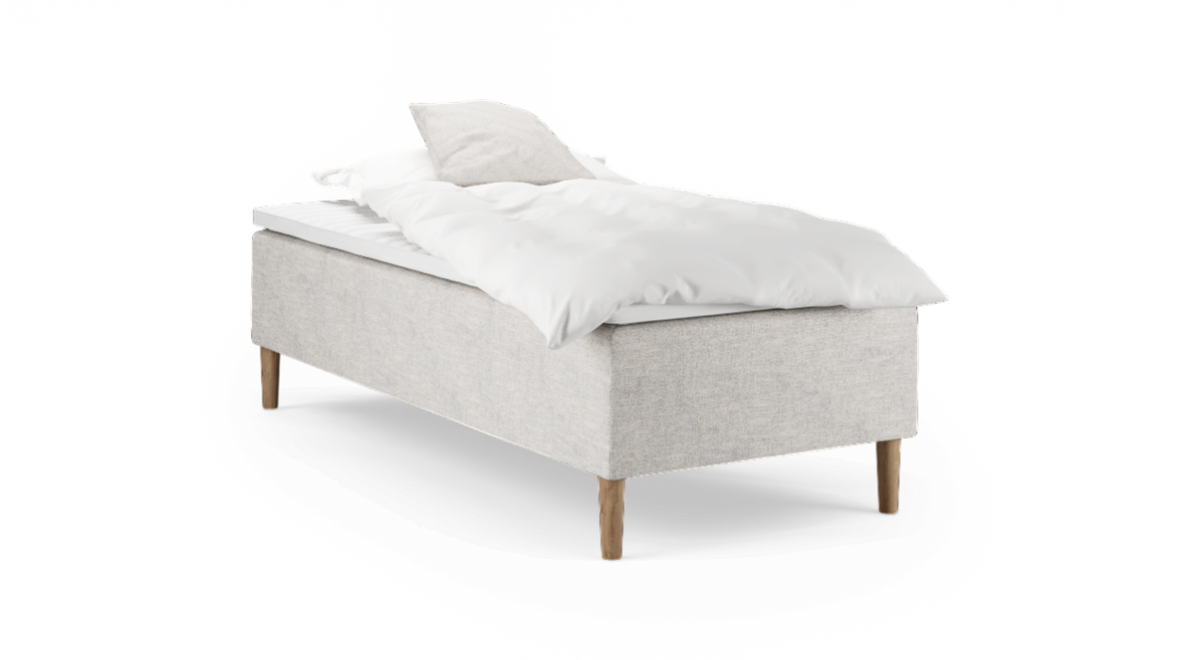 Enkelbädd med ljusbeige tygklädd bas, träben samt vit kudde och täcke, frilagd mot svart bakgrund.