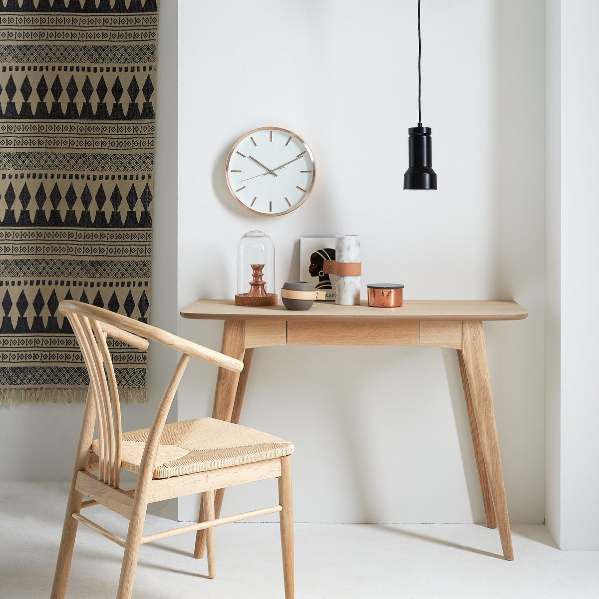 Ljus träskrivbord med stol, väggklocka och svart pendellampa i ett skandinaviskt, minimalistiskt arrangemang.