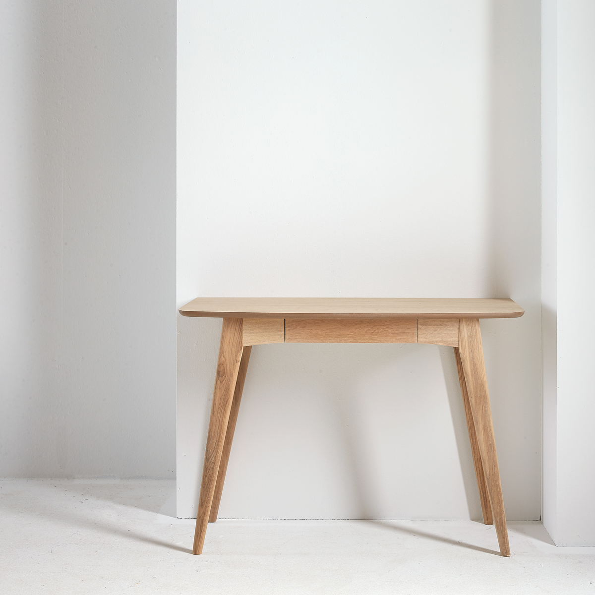 Konsolbord i ljust trä med avsmalnande ben mot en vit, minimalistisk vägg.