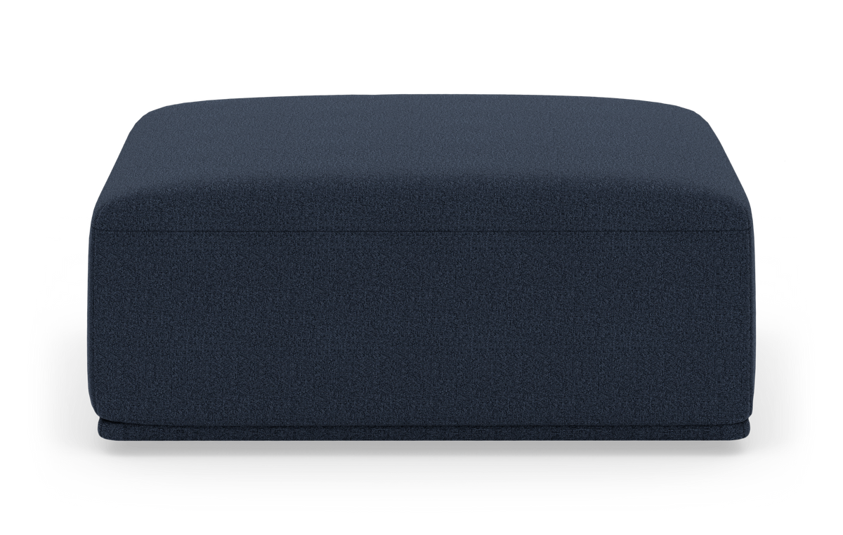 Mörkblå rektangulär sittpuff/ottoman i tyg sedd rakt framifrån på vit studiobakgrund.